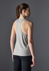 Grå idrettstopp med racerback-design, myk tekstur og figurklemende silhuett, sammen med svarte leggings, sett fra bak.
