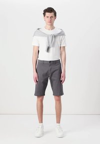 Graue Shorts aus Baumwolle mit flachem Bund und Gürtelschlaufen, kombiniert mit einem weißen T-Shirt. Ein hellgrauer Pullover ist lässig über die Schultern gelegt.