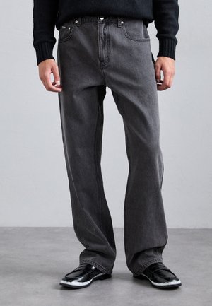 Grå denimjeans med rett ben, med synlige sømmer og frontlommer, kombinert med glansfulle svarte sko.