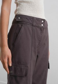 Dark brown cargo pants with a high waist, featuring side pockets, visible stitching, and metallic button accents at the top.