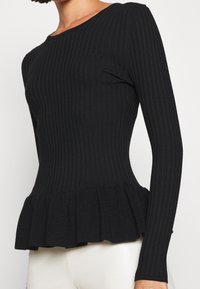 Black ribbed long-sleeve top with a peplum hem, showcasing textured fabric and a fitted bodice. Round neckline and subtle flare at the waist.