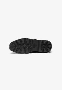 Schwarze Gummistiefelsohle mit tiefem Profilmuster, versehen mit einem Logo an der Seite und einem robusten Design für Grip und Langlebigkeit.