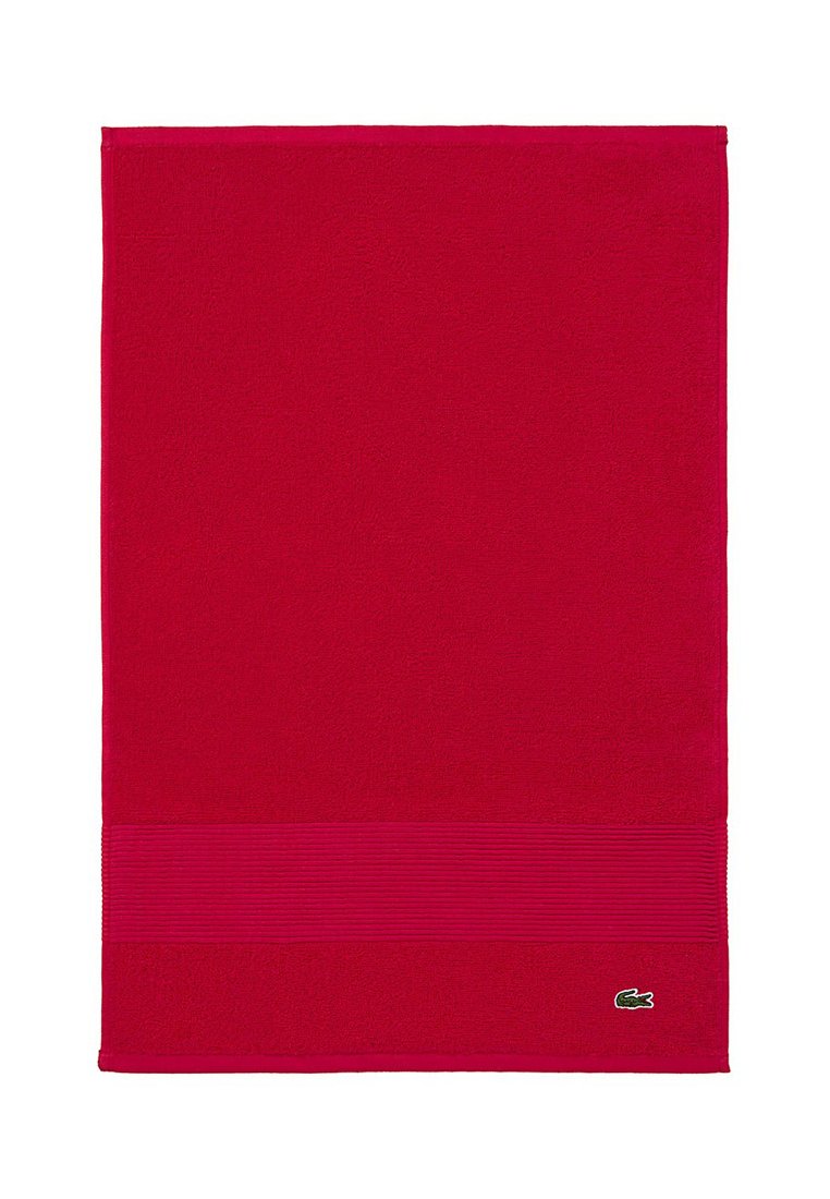 Toalla de algodón roja con un detalle de raya horizontal texturizada en la parte inferior y un pequeño logo verde en la esquina. Forma rectangular.