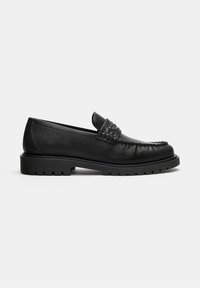 Mocassin en cuir noir avec semelle crantée épaisse, détails surpiqués et bride cloutée sur le dessus, présenté en profil latéral sur fond blanc.