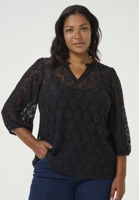 Top en dentelle noire avec un décolleté en V, des manches bouffantes 3/4 et des motifs floraux. Fabriqué à partir d'un matériau transparent avec un ourlet arrondi et une coupe décontractée.