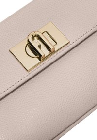 Jasnoróżowa skórzana kopertówka o teksturowanej powierzchni, z zapięciem z złotego metalu z detalem logo. Gładkie krawędzie i czyste linie.