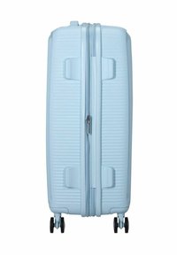 Valigia azzurra chiara con texture a righe verticali, chiusura zip e due ruote nere. Il manico è integrato per un facile trasporto.