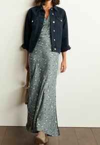 Chaqueta de mezclilla con mangas enrolladas sobre un vestido maxi floral verde con patrones morados y blancos, combinada con botines de plataforma beige.