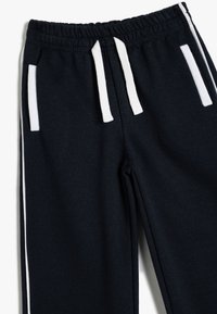 Pantalones de chándal de color azul marino oscuro, hechos de una tela suave, con franjas laterales blancas, cintura elástica y bolsillos frontales con ribete en contraste.