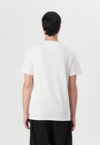 T-shirt en coton blanc à manches courtes, coupe droite, avec un petit détail en V au niveau du col à l'arrière. Texture simple et lisse.