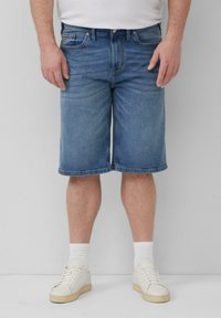 Szorty dżinsowe w jasnoniebieskim odcieniu, do kolan, z niebieskimi przeszyciami, kieszeniami z przodu i klasycznym pięciokieszeniowym wzorem, w połączeniu z białymi trampkami.
