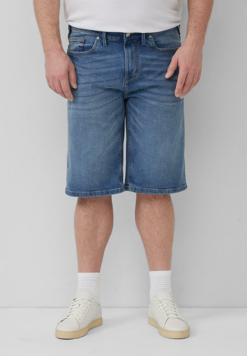 Szorty dżinsowe w jasnoniebieskim odcieniu, do kolan, z niebieskimi przeszyciami, kieszeniami z przodu i klasycznym pięciokieszeniowym wzorem, w połączeniu z białymi trampkami.