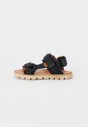 Schwarze Stoffsandalen mit verstellbaren Riemen, einer strukturierten Sohle und einer braunen Innensohle. Merkmale ein leichtes Design und ein robustes Profil.