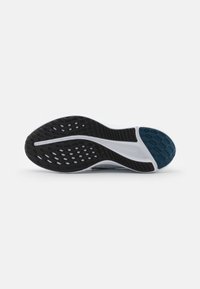 Suela de zapato de goma negra con un patrón texturizado, que presenta una entresuela blanca y un acento en verde azulado cerca del talón.