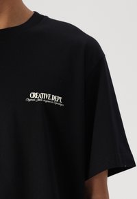 Sort bomuld t-shirt med en afslappet pasform. Har et hvidt grafisk print "CREATIVE DEPT." på venstre bryst. Korte ærmer og rund halsudskæring.