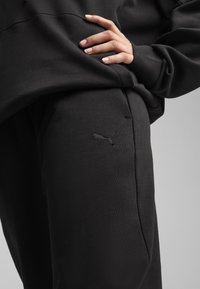 Sorte sweats med blødt stof har et broderet Puma-logo på låret, med en afslappet pasform og subtile teksturdetaljer.