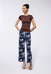 Maglietta marrone aderente a maniche corte abbinata a pantaloni larghi blu navy con una stampa floreale bianca, tessuto morbido e sandali aperti.