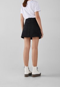 Black denim skirt with a flared shape, high waist, and two back pockets, paired with a white t-shirt and white ankle boots.