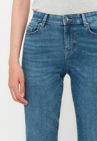 Blaue Denimjeans mit geradem Schnitt, sichtbar Reißverschluss, Knopfverschluss und Vordertaschen. Leicht verwaschener Stoff.