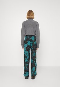 Grijze trui met hoge hals gecombineerd met wijde broek met een gedurfd turquoise en zwart bloemenpatroon. De textuur oogt zacht en ontspannen.