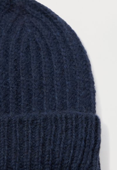 Diepblauwe gebreide beanie met een geribbelde textuur, die een zachte, fuzzy uitstraling en een omgeslagen manchet aan de onderkant toont.
