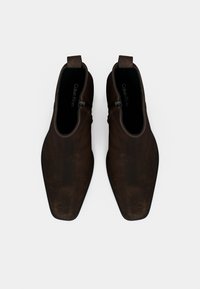 Brazne usnjene gležnjarje z gladko teksturo, koničastim nosom in stranskimi zadrgami. Notranjost obložena s črnim materialom, s logotipom vidnim znotraj.