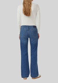 Jean en denim bleu évasés avec un design à cinq poches et une taille foncée, offrant un look légèrement délavé et des détails d'ourlet effilochés.