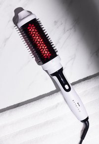 Haarstylingbürste mit einem schwarz-roten Barrel, Kunststoffborsten und einem weißen ergonomischen Griff. Verfügt über einen Netzschalter und ein Kabel.