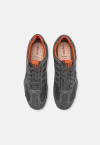 Grey athletic shoes with suede and mesh materials, featuring orange accents and a perforated design for breathability. Laced closure.