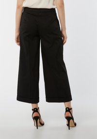 Pantalones de pierna ancha negros con un acabado suave, puños enrollados y una cintura de altura media, combinados con sandalias negras de tacón alto.