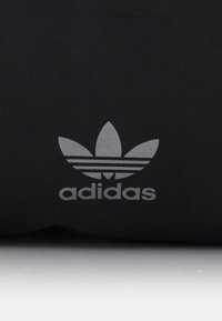 Black fabric with a subtle textured pattern; features a silver Adidas logo with three leaf-like accents above the brand name.