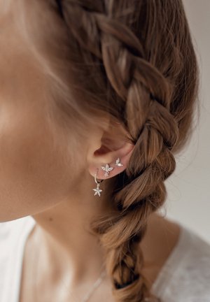 Silberohrringe mit floralem Design und mehreren Edelsteinen, einschließlich einer Hängering- und Stecker-Variante, getragen zu einem geflochtenen Haarschnitt.