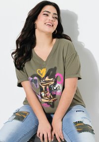 T-shirt olive vert en v avec un imprimé graphique représentant un crocodile, rehaussé de éclaboussures colorées de rose et de jaune. Assorti avec un jean déchiré.