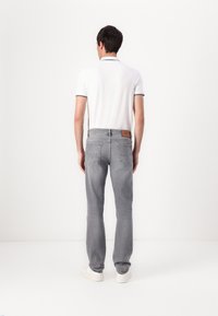 Pilkos džinsinės kelnės su siauru siluetu, su odiniu ženkleliu gale, derinamos su balta polo marškinėliais su juodu apvadu.