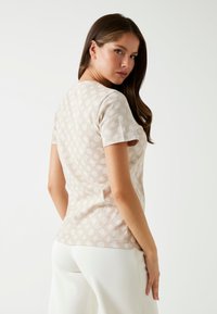 Korte mouwen beige t-shirt met een licht patroon van cirkels en bloemenmotieven; zachte stof, slim fit en ronde hals.