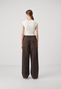 Mørkebrune vidde jeans med høy midje og to baklommer; kombinert med en tettsittende hvit ribbestrikket tanktop, sett fra baksiden.