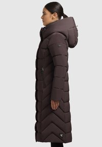 Długa, ciemnobrązowa puchowa kurtka z przeszyciami w kształcie szewrona, wysokim kołnierzem i regulowanym kapturem. Posiada zapinane na zamek boczne kieszenie i logo.