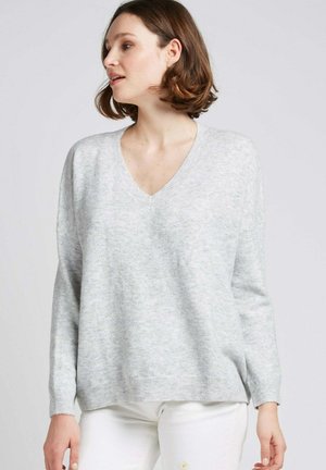 Pull en maille doux, gris clair, avec un col en V, des épaules tombantes et un ourlet côtelé. Design simple sans motifs ni matériels visibles.