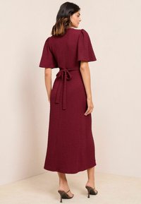 Abito midi bordeaux caratterizzato da un tessuto testurizzato, maniche corte a sbuffo e una cintura legata in vita. Il design presenta una silhouette fluida e morbida.