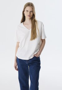 Weißes V-Ausschnitt-T-Shirt aus leichtem Stoff, kombiniert mit lässigen blauen Jeans. Das T-Shirt hat kurze Ärmel und eine lockere Passform.