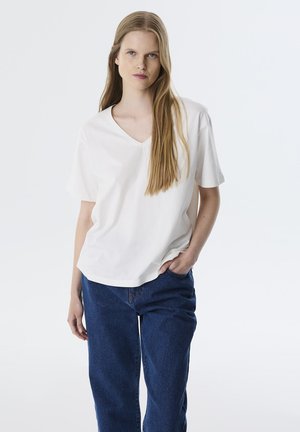Witte V-hals t-shirt van lichtgewicht stof, gecombineerd met een relaxte spijkerbroek in het blauw. Het t-shirt heeft korte mouwen en een losse pasvorm.