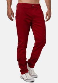 Pantaloni di cotone rossi con design slim-fit, dotati di chiusura con bottone, tasche frontali e una texture liscia. Abbinati a sneakers bianche.