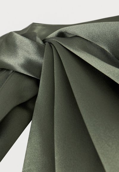 Σκούρο πράσινο μεταξένιο ύφασμα, διπλωμένο και μαζεμένο σε απαλές πτυχές, τονίζοντας την ομαλή υφή και τη διακριτική γυαλάδα.