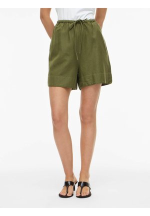 Femme portant un short vert olive à cordon de serrage et des sandales à talons noires à bouts ouverts, debout devant un fond blanc.