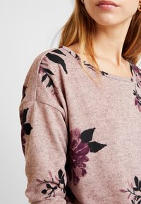 Heller rosa Blumen-Sweatshirt mit dunklen Blättern und mauvefarbenden Blumen, in lockerer Passform und mit weitem Ausschnitt. Weicher, strukturierten Stoff.