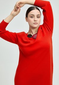 Rotes Strickkleid mit rundem Ausschnitt, langen Ärmeln und lockerem Schnitt. Verfügt über eine klobige Halskette mit kreisförmigen Akzenten.