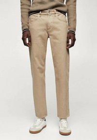 Beige, gerade geschnittene Jeans mit fünf Taschen und Gürtelschlaufen. Getragen mit weißen Sneakern mit beigen Akzenten und einem weißen Strickpullover.