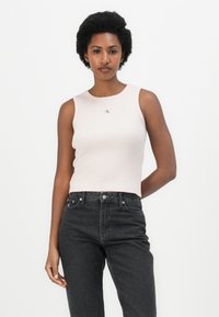 Top a maniche lunghe ribelle di colore rosa chiaro con scollatura tonda e una piccola etichetta con logo, abbinato a jeans in denim scuro a vita alta.