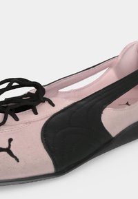 Крупен план на розовo и черно маратонка Puma с черни връзки и черно лого на Puma в областта на пръстите.