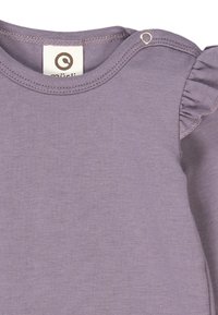 Fialový bavlněný top s kulatým výstřihem, který má malou patentku a volánkové detaily na rukávech. Měkká, hladká textura.